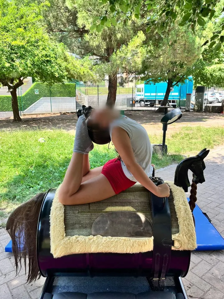 Una ragazza in equilibrio su una sella-gioco a forma di pony, all’aria aperta